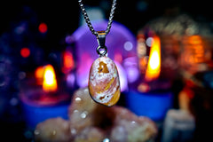 Necklace with a pendant featuring a natural stone design, set against a blurred background with candles and stones.