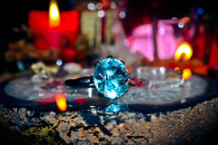 Blue gemstone ring on a dark surface with blurred candles and lights in the background