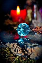 Blue gemstone ring on a reflective surface with a candle in the background