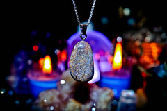 Necklace with a glittery pendant against a mystical background with candles and crystals.