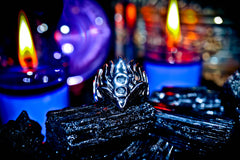 Metallic hand-shaped object with a central emblem, surrounded by candles in a dark setting