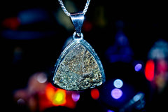 Genie Amulet Maymun Triangular diamond pendant on a chain against a blurred colorful background