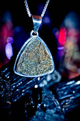 Maymum King Djinn Triangular pendant with textured surface on a chain against a blurred background