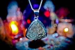 Maymun King Djinn Necklace with a large, textured pendant against a blurred background with lights.